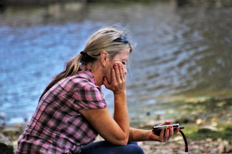 mature woman thinking at water's edge with phone ryan fahlen