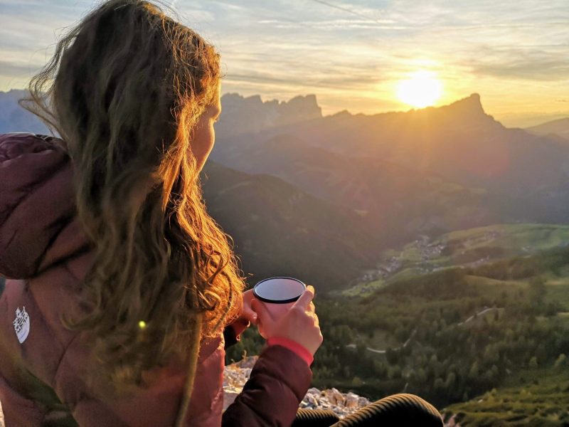 woman staring into distant valley in mountains holding coffee