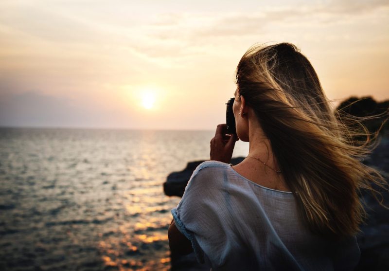 woman looking out over ocean with camera andhair blowing room for content fahlen ryan