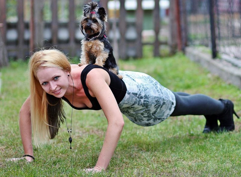 woman doing pushup with dog on her back