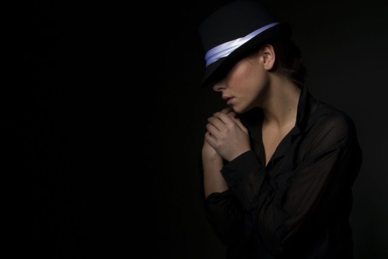 woman wearing dark hat on dark background space for copy