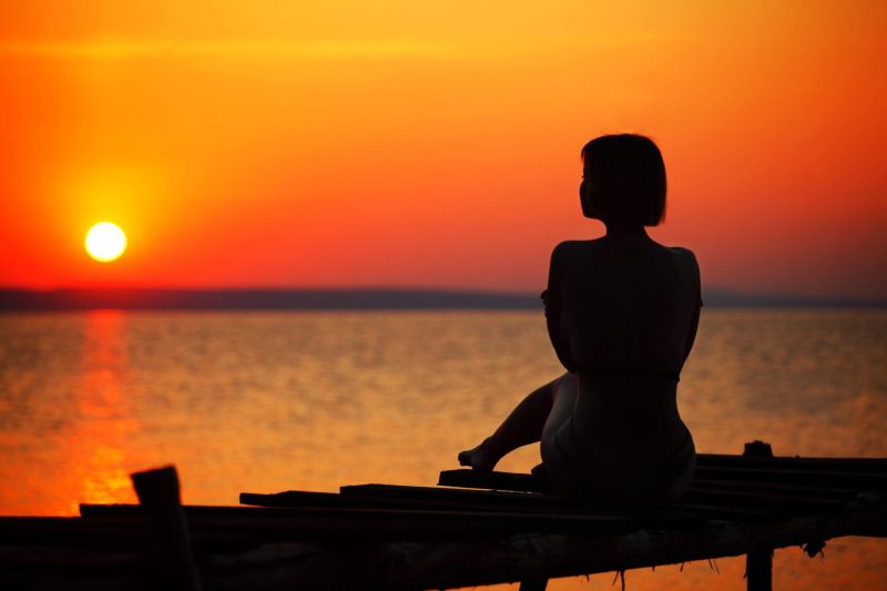 woman on crude pier overlooking bay at sunset